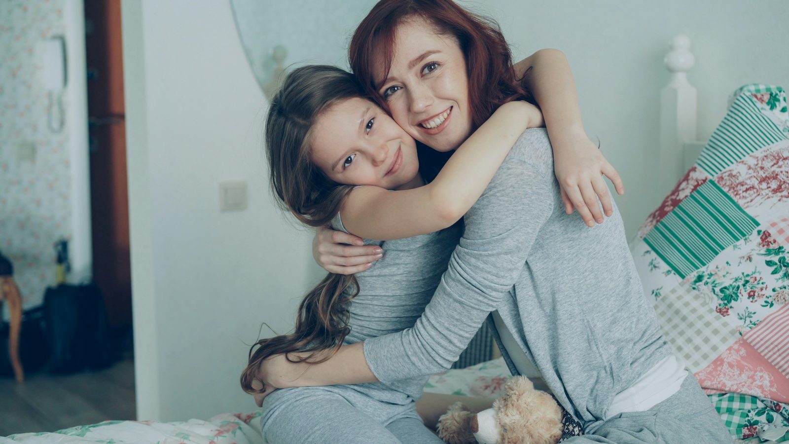 A mother and her daughter sharing a warm hug while sitting together on a bed